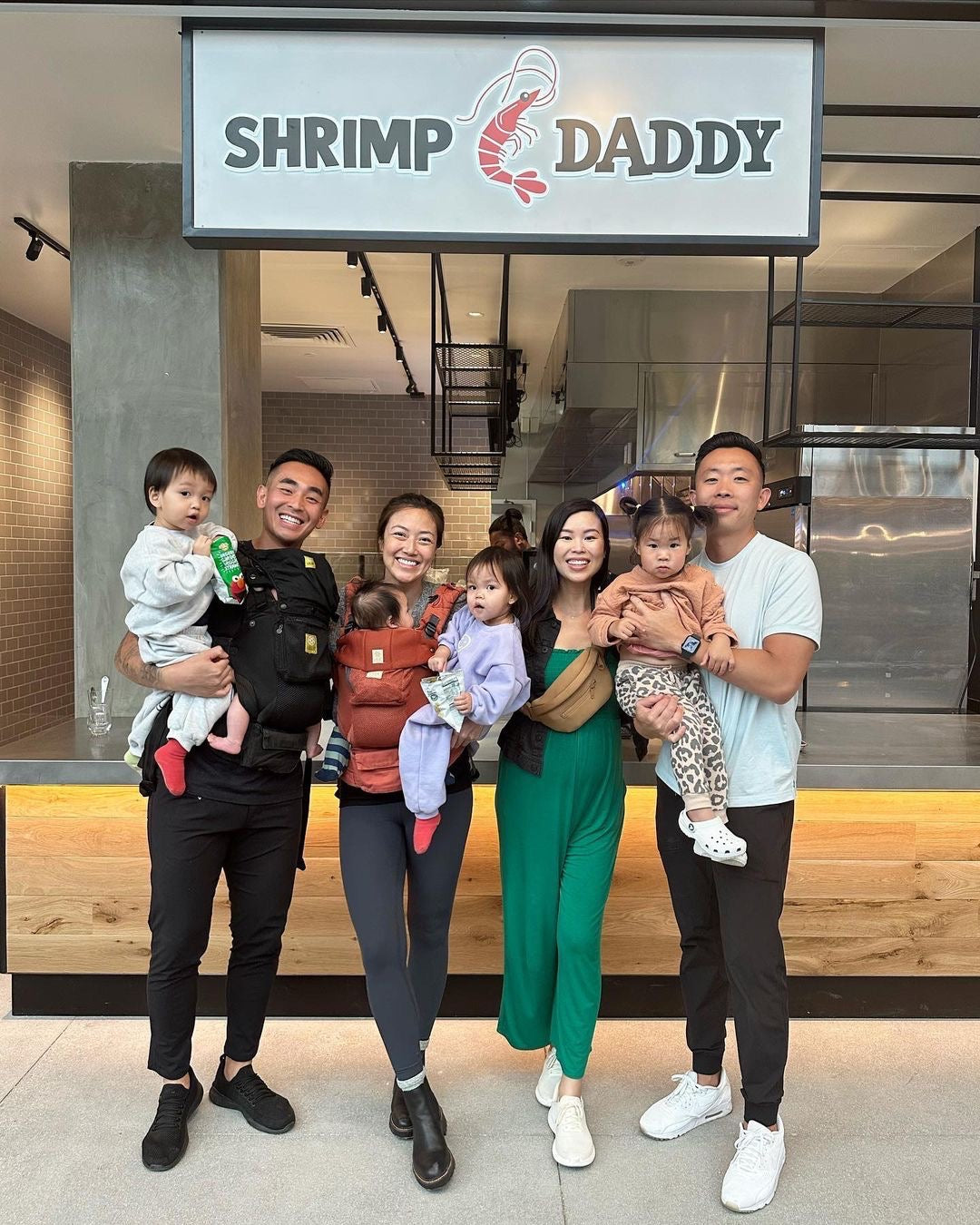 4 smiling adults holding their children while at the Topanga, CA location of Shrimp Daddy